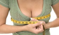 Picture of a woman, happy with her perfect breast reduction procedure she had with Top Plastic Surgeons in beautiful Cabo San Lucas, Mexico.  The woman is facing the camera, measuring her breasts with a tape measure,  and wearing an olive colored blouse