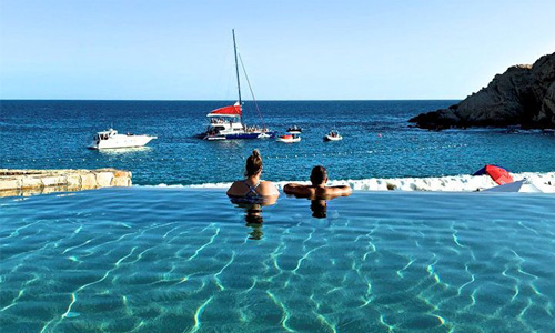 Picture of beautiful beach in Los Cabos, Mexico.  The picture shows  a couple looking into the ocean from the pool.