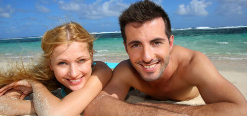 Picture of a smiling couple showing their happiness with their visit to Los Cabos for plastic surgery.  The woman is resting her head on her arm and both are facing the camera with a big smile.