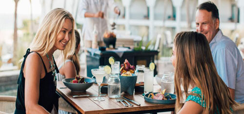 Picture of a happy guest dining in Cabo San Lucas, Mexico.  The picture is of an attractive woman with long sandy blonde hair, wearing a black blouse, and sitting at a table with companions.