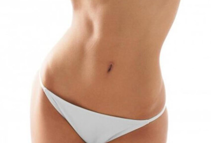 Picture of a woman facing the camera and happy with the perfect abdomen liposuction procedure she had with top plastic surgeons in beautiful Cabo San Lucas, Mexico.  She is wearing a two piece bikini and showing a flat abdomen to the camera.