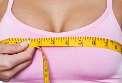 Picture of a woman measuring her breasts with a tape measure, and happy with the perfect breast reduction procedure she had with  top plastic surgeons in beautiful Cabo San Lucas, Mexico.  She is wearing a light purple top and facing the camera.