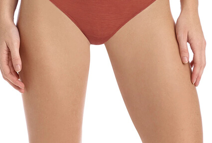 Picture of a trim woman wearing a red bikini bottom, and happy with her perfect thigh lift she had with top plastic surgeons in beautiful Cabo San Lucas, Mexico.  The woman is facing the camera with both arms down to her sides.