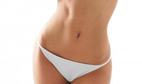 Picture of a woman facing the camera and happy with the perfect abdomen and waist liposuction procedure she had with Cabo MedVentures in beautiful Cabo San Lucas, Mexico.  She is wearing a two piece bikini and showing a flat abdomen to the camera.