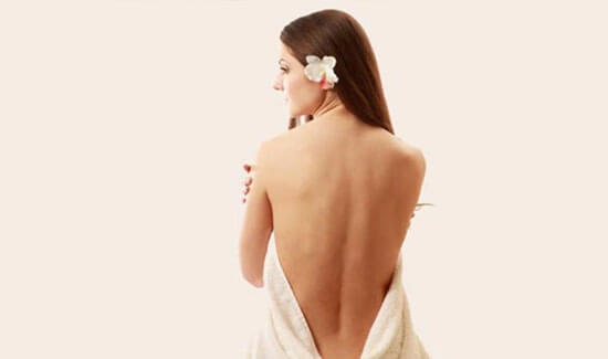 Picture of a woman sitting with her back to the camera and happy with her perfect back liposuction procedure she had with Cabo MedVentures in beautiful Cabo San Lucas, Mexico.  The woman has a white towel draped around her.
